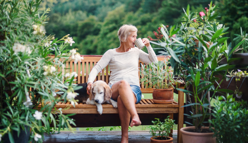 Woman sits on bench with dog while drinking out of a mug.